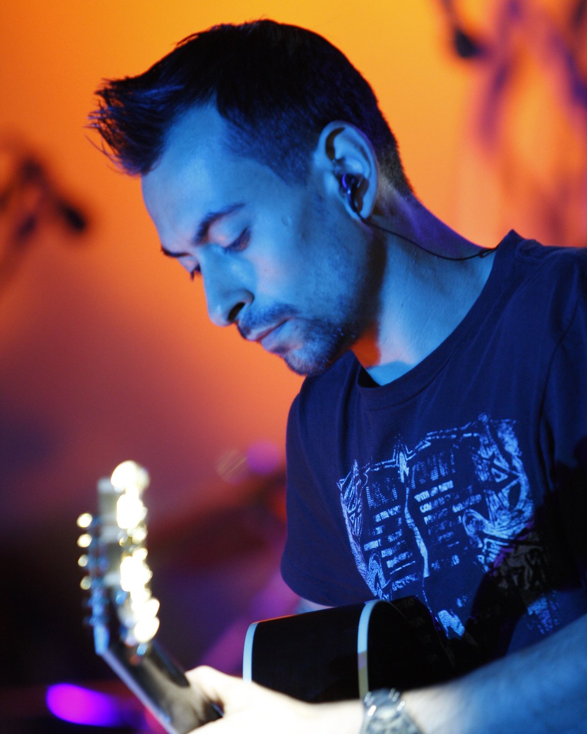Alex Bodnar playing acoustic guitar under orange and blue stage light