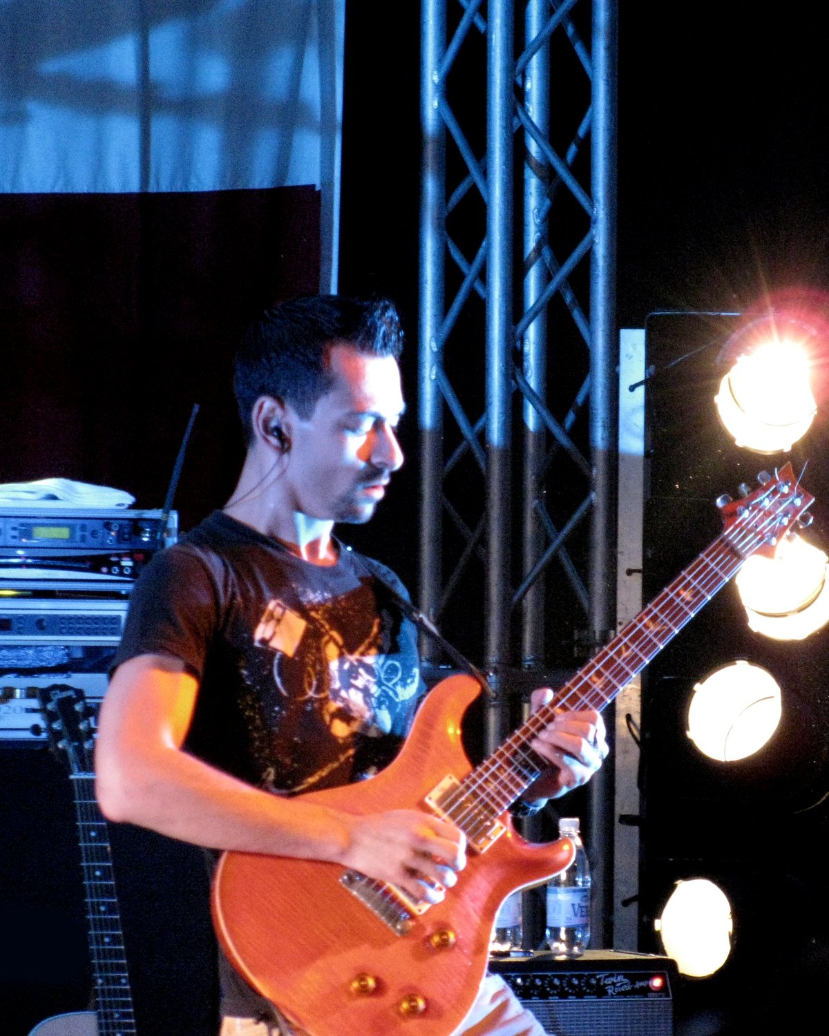 Alex Bodnar playing an orange PRS guitar beside stage lights