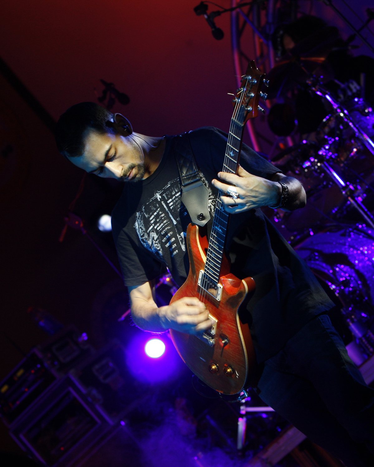 Alex Bodnar playing a red PRS guitar under purple stage light