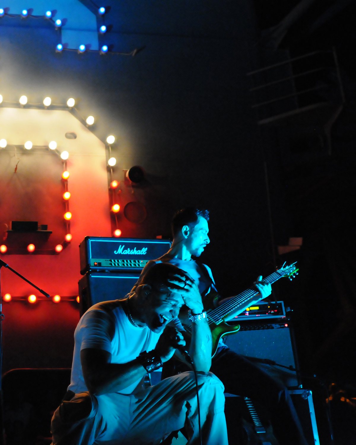 Scott Stapp kneels mid-song as Alex Bodnar plays guitar behind him on stage aboard the USS Ronald Reagan